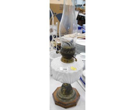 A brass oil lamp, with opaque white glass reservoir, on an oak base.
