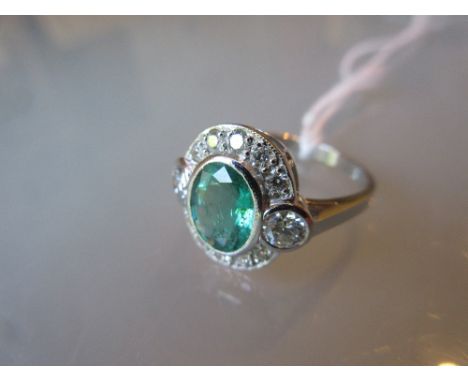 Art deco style emerald and diamond ring of oval design with diamond set shoulders, the central emerald of approximately 0.75c