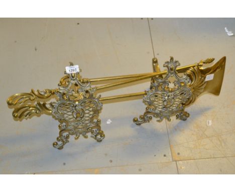 Pair of ornate brass fire dogs together with two fire tools and a brass lamp base