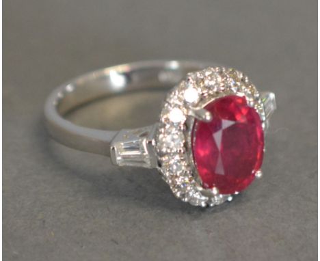 An 18ct. White Gold Ruby and Diamond Cluster Ring, with an oval ruby surrounded by diamonds within a pierced setting