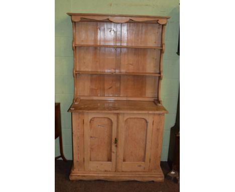 A Victorian pine kitchen dresser, the rack with two shelves, the base of two moulded cupboard doors enclosing a shelf, on a m