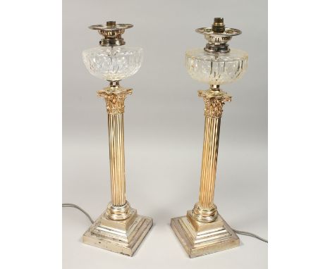 A GOOD PAIR OF CORINTHIAN COLUMN SILVER PLATED OIL LAMPS, each with a cut glass reservoir, converted to electricity. 25ins hi