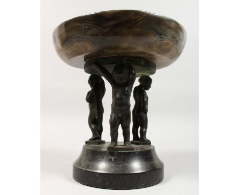 A BRONZE AND SIMULATED MARBLE COMPORT, supported by three bronze cherubs. 9ins diameter.