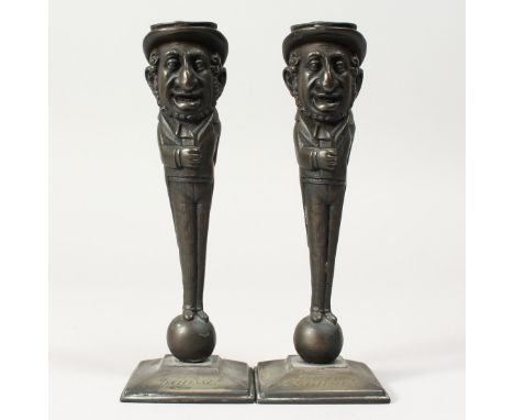 A PAIR OF JUDAICA BRONZE CANDLESTICKS of men, the hat as a candle holder, the man standing on a sphinx and square base. Inscr