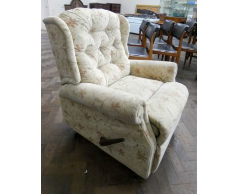 A manual reclining wing backed easy chair in cream floral covering  