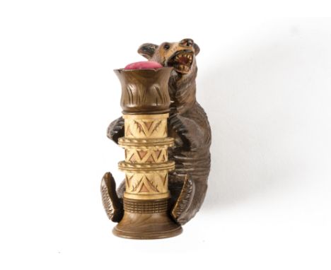 A circa 1930s black forest carved bear, lying on back juggling a detachable bobbin holder with pin cushion inserted to the to