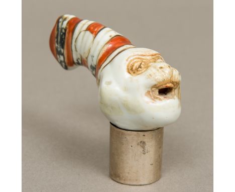 A Victorian porcelain walking stick handleFormed as a monkey wearing a hat; together with a loose silver collar.  8 cm long. 