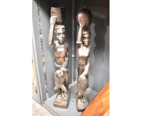 A pair of carved hard wood African tribal sculptures each carrying fish and vessels, h69cm