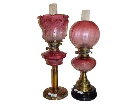 An Art Nouveau brass based oil lamp with cranberry glass font and etched shade, together with another similar Victorian oil l