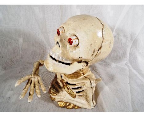 A cast iron novelty money bank in the form of a skull and partial skeleton