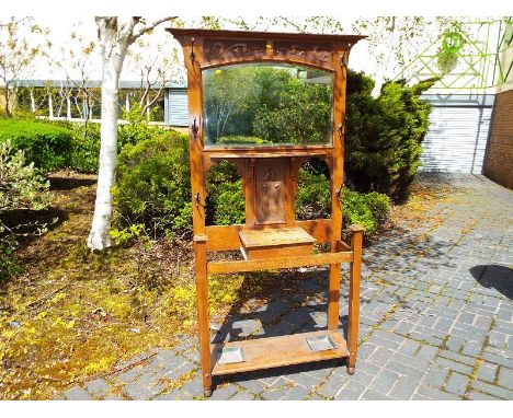 An Art Nouveau oak mirror back hall stand with central shelf and opening storage box, coat hooks and umbrella / stick trays, 