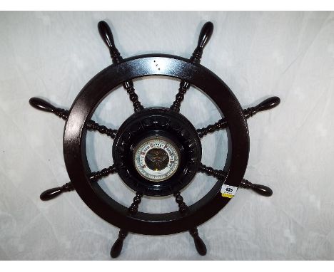 A wall mounted aneroid barometer in the form of a ships wheel, white enamel dial with open centre showing the mechanism Est £