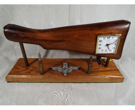 A desk alarm clock in the form of a rifle stock on a wooden pedestal, enhanced by two bullets and cast insignia Est £20 - £30