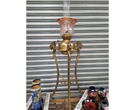 A FLOOR STANDING OIL LAMP, THE BRASS RECEIVER CRADLED BETWEEN THREE DRAGONS HEADS AT THE TOP OF THREE SABRE SHAPED LEGS