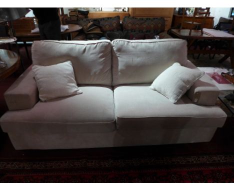 A contemporary designer two seater sofa of angular form upholstered in beige fabric raised on black supports with additional 