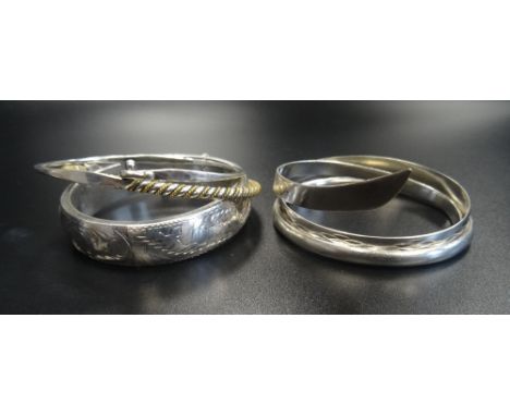 SIX SILVER BANGLESof various designs, including a floral and scroll engraved hinged bangle with safety chain and another with
