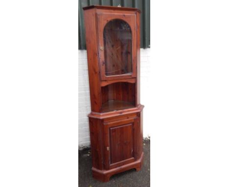 A modern stained pine standing corner cabinet, the upper section enclosed by a single glazed door and with open shelf, the st