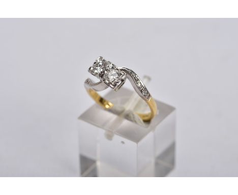 AN 18CT GOLD DIAMOND CROSS OVER RING, designed with two asymmetrical set round brilliant cut diamonds, each within a square m