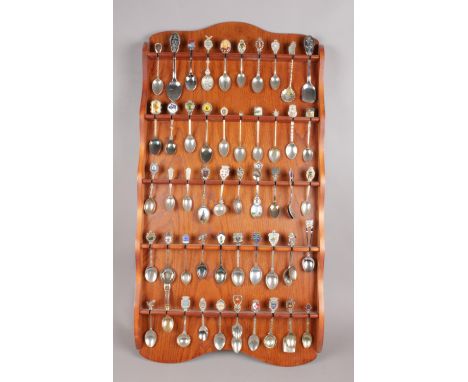 An oak display rack with contents of collectors spoons. Some spoons with enamel decoration. (approximately 53 spoons).  