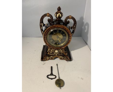 AN ORNATE TREACLE GLAZED MANTLE CLOCK WITH KEY (REPAIR TO DECORATION) 