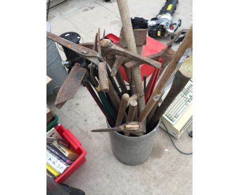 A STAINLESS STEEL STORAGE BUCKET CONTAINING A LARGE ASSORTMENT OF GARDEN TOOLS TO INCLUDE AXES, A SYTHE AND PICK AXES ETC 