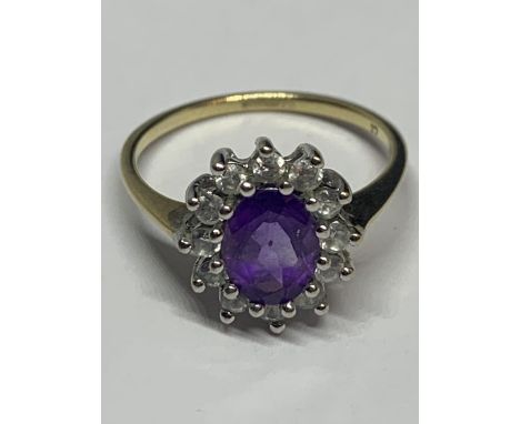 A 9 CARAT GOLD RING WITH A CENTRAL AMETHYST SURROUNDED BY CLEAR STONES SIZE O IN A PRESENTATION BOX 