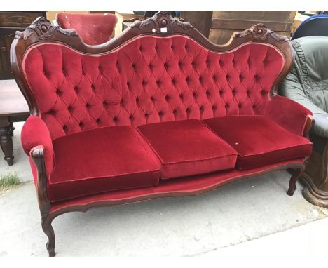 A FRENCH STYLE CARVED WOODEN AND RED BUTTON BACK UPHOLSTERED THREE SEATER SOFA 