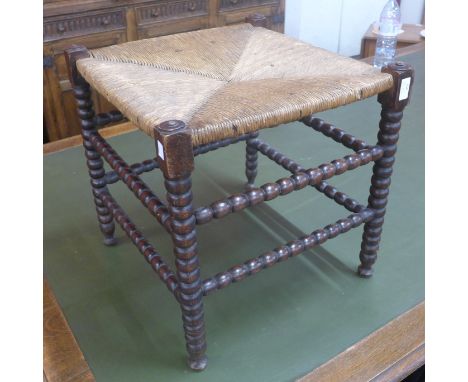 An Arts and Crafts ebonised bobbin turned and rush seated stool 
