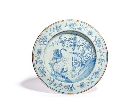 A Liverpool delftware charger  c.1760, painted with two European travellers seated beneath flowering branches and gesticulati