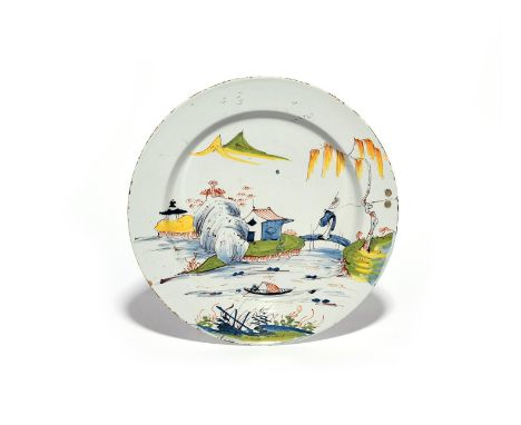 A delftware plate or charger  c.1750-60, decorated in polychrome enamels with a figure crossing a bridge to a hut on an islan