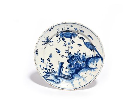 A delftware plate  mid 18th century, decorated in a deep blue with an exotic bird perched atop of rocks before flowering plan