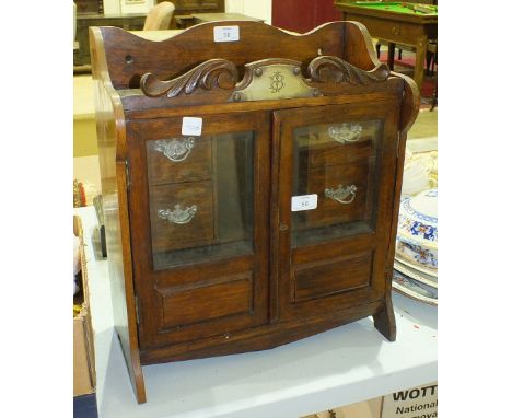 An Edwardian oak smokers' hanging wall cabinet with a pair of glazed doors, four small drawers, shelf and pipe rack, 40.5cm w