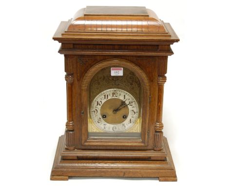 A late 19th century continental oak cased mantel clock having an arched brass dial with silvered chapter ring and Arabic nume