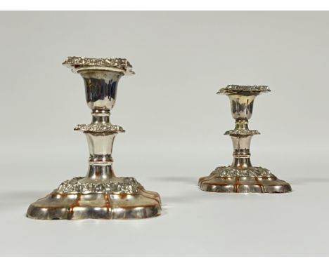 A pair of silver plated Rococo style candlestick holders raised on square supports with low-relief moulded scroll decoration 