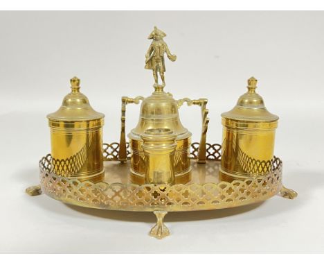 A lacquered brass ink stand or desk set comprising a candlestick holder, two inkwells, and a central compartment with bell as
