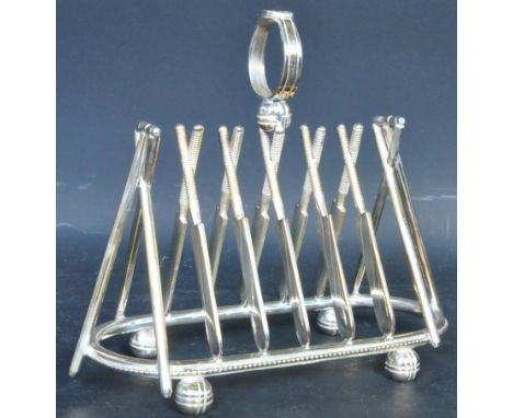 A silver plated toast rack in the form of a series of crickets bat with ring handle raised upon bun feet. Measures 16cm x 16c
