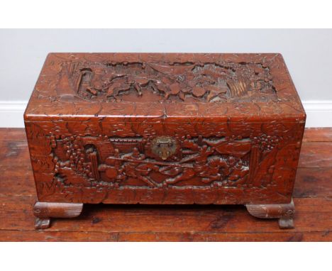 A Chinese camphor wood trunk, ornately carved with scenes of figures and horses battling, raised on shaped bracket feet, 78cm