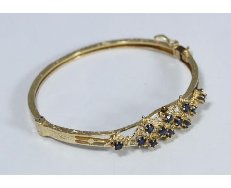 A 14ct gold hinged bangle, claw-set to the top with 12 small round facetted Sapphires, 12.80 grams 