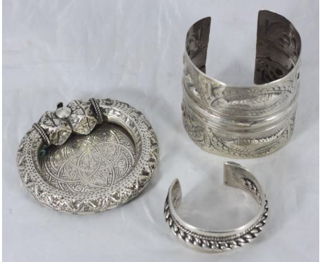 An Ottoman white-metal cuff bangle, embossed with lunettes and fish, together with an Egyptian white metal torque bangle and 