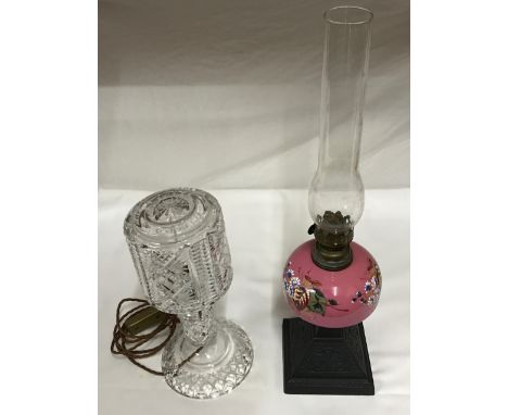 Two table lamps, one heavy cut glass in two sections 36cms h. Pink glass oil lamp with floral painted design 62cms h to top o