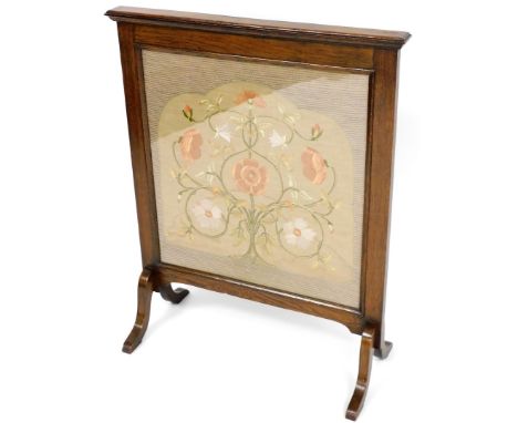 A Victorian needlework fire screen, in a later oak surround, the central panel in silver depicting pink and cream flowers on 