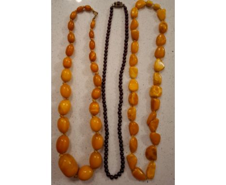 Three vintage necklaces comprising a garnet bead necklaces with white metal clasp and 2 egg yolk amber effect bead necklaces.