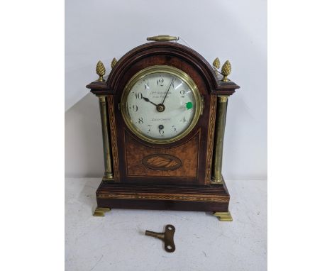 An early 20th century mahogany mantel clock with an eight day chain fusee movement, a handle to the arched top, four acorn fi