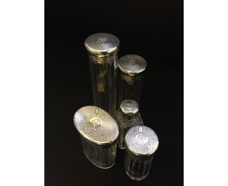 Set of five cut glass dressing case bottles with engine turned silver lids. 