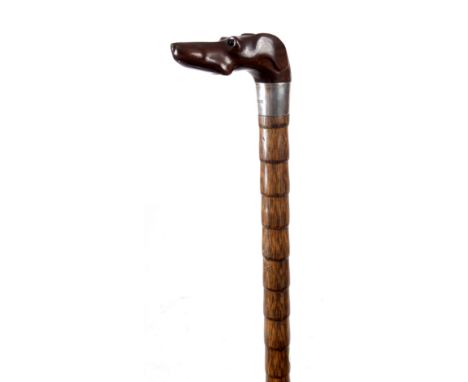 AN EARLY 20th CENTURY CARVED COROMANDEL DOGS HEAD HANDLED WALKING CANE formed as a greyhound with amber glass eyes mounted on