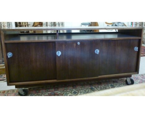 A 1970s rosewood finished sideboard, having an open, shallow frieze shelf, over three lockable, sliding, in-line drawers with