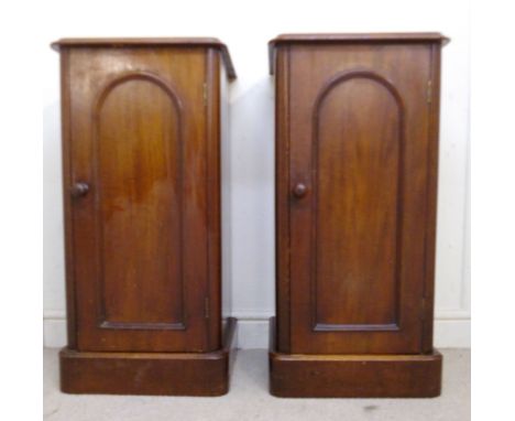 A pair of late Victorian mahogany bedside cabinets, each having a low upstand, over an arched, panelled door, enclosing a she