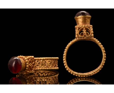 Ca. AD 600. An elegant gold ring with a flat-section hoop with applied beaded wire borders. The bezel has a raised architectu