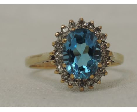 A lady's dress ring having an oval blue topaz and diamond chip cluster in a claw set mount on a 9ct gold loop, size M