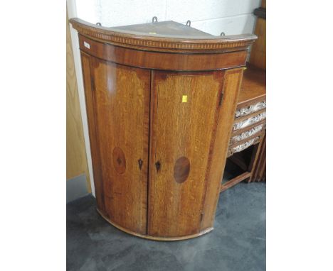 A late 18th/early 19th century George III golden oak corner wall cupboard having bow front and mahogany inlay and crossband d